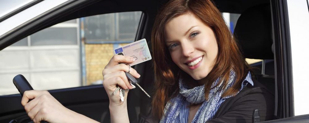 Uśmiechnięta kobieta za kierownicą pokazuje prawo jazdy
